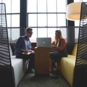 Two adults discussing work and collaborating in a modern office lounge area.