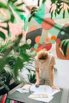 A focused woman reviews documents in a lush, colorful workspace adorned with abstract art.